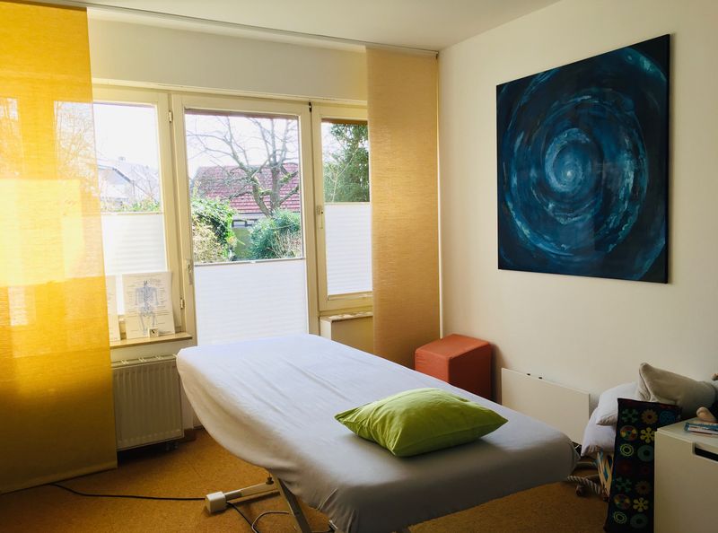 Behandlungsraum der Praxis mit Liege, grünem Kissen und einem blauen Gemälde an der Wand
